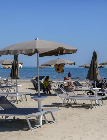 Spiaggia con ombrelloni grigi, sedie a sdraio e persone che si rilassano.