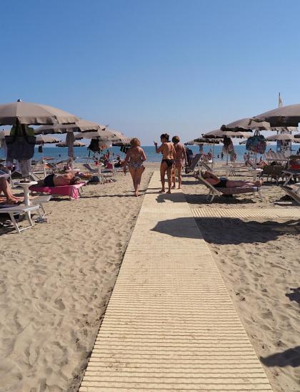 Überfüllter Strand mit Sonnenschirmen und Liegen unter klarem Himmel.