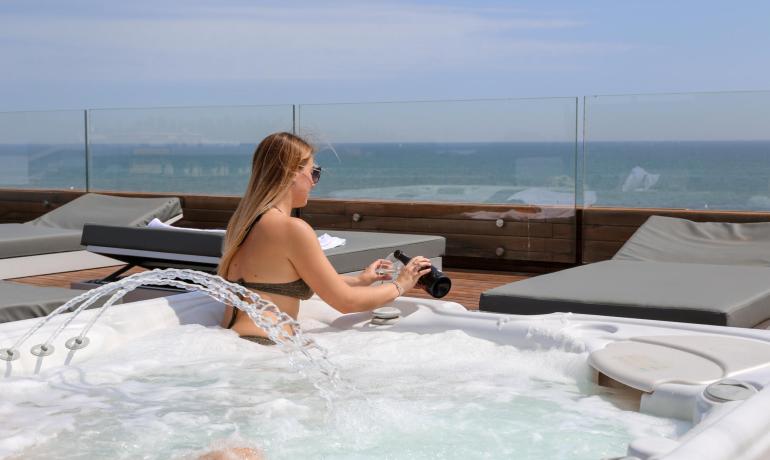 Frau im Jacuzzi mit Meerblick, gießt aus einer Flasche.