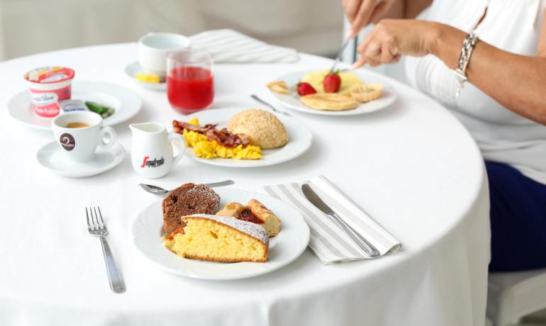 Colazione con dolci, uova, pancetta e caffè su tavola apparecchiata.