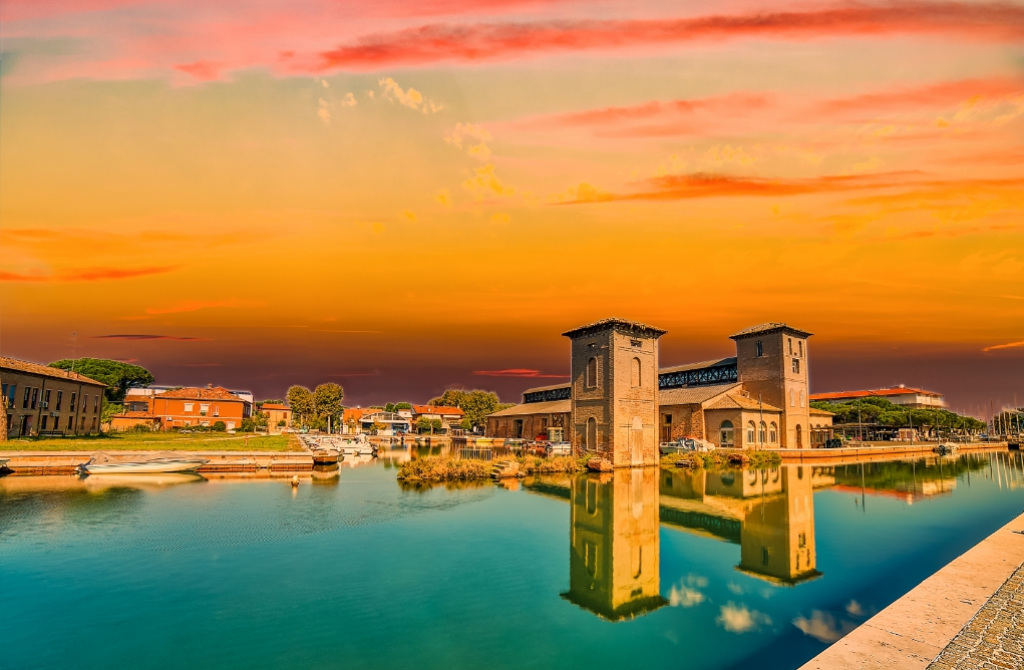 Tramonto su edifici storici riflessi nell'acqua, con cielo arancione vibrante.