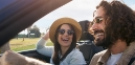 Due persone sorridenti viaggiano in auto decappottabile sotto il sole.