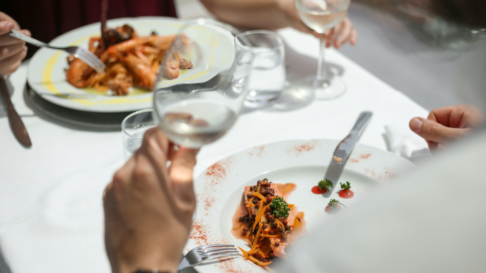 Cena elegante con piatti gourmet e calici di vino bianco su tavola apparecchiata.