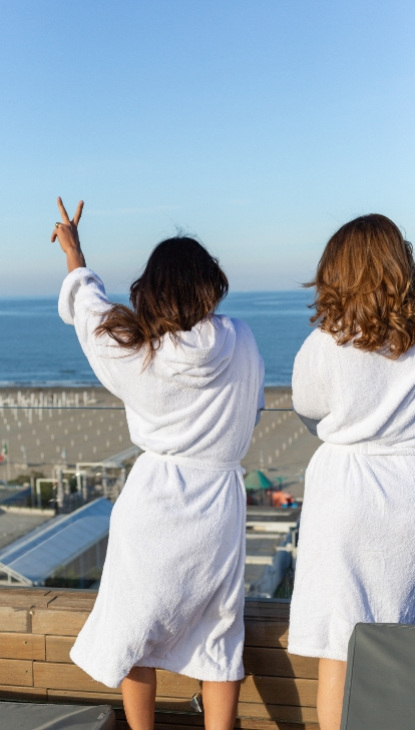 Due persone in accappatoio guardano il mare da una terrazza.