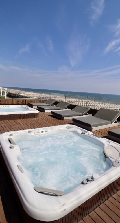 Vasca idromassaggio all'aperto con vista mare, lettini prendisole su terrazza in legno.