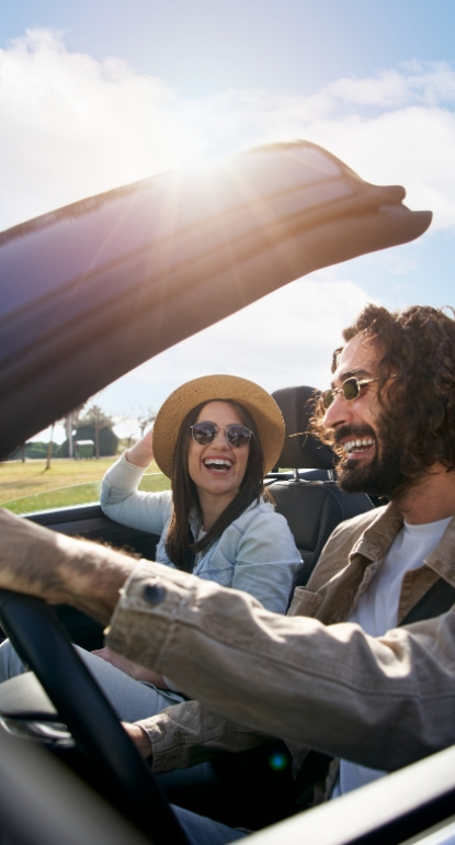 Coppia felice guida una decappottabile sotto il sole, sorridendo e godendosi la giornata.