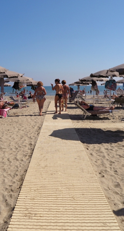 Spiaggia affollata con ombrelloni e lettini, persone che si rilassano al sole.