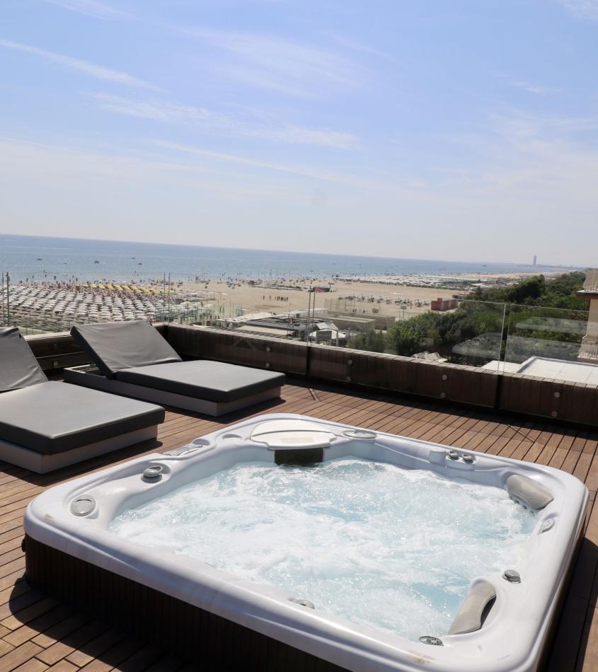 Terrazza con vasca idromassaggio e vista mare, lettini prendisole sullo sfondo.