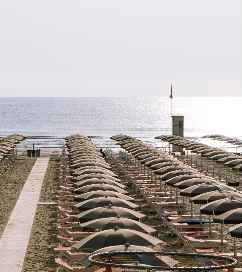 Spiaggia con file di ombrelloni chiusi e mare calmo sullo sfondo.