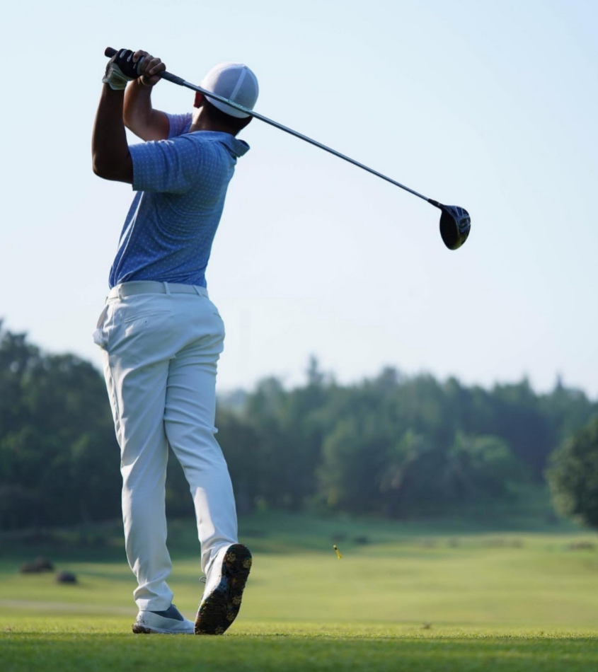 Golfista in azione con il driver su un campo verde e soleggiato.