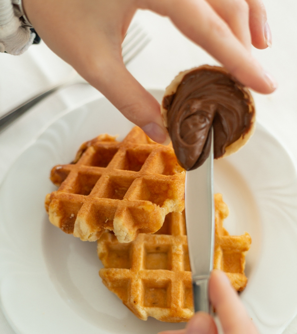 Waffle con crema al cioccolato spalmata con un coltello su un piatto bianco.